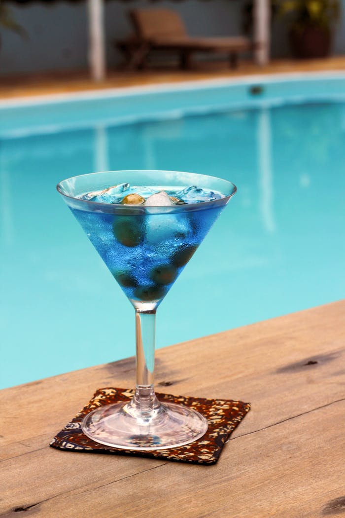 A cool blue cocktail sits invitingly by a swimming pool, perfect for summer relaxation.