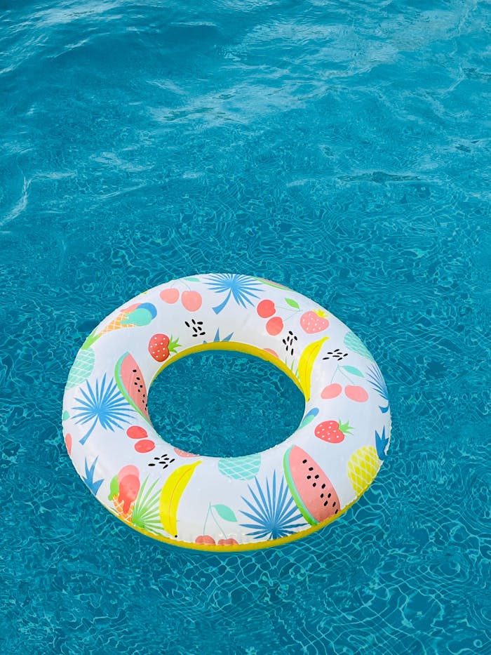 Vibrant inflatable pool ring with a fruity print floats in clear blue water.