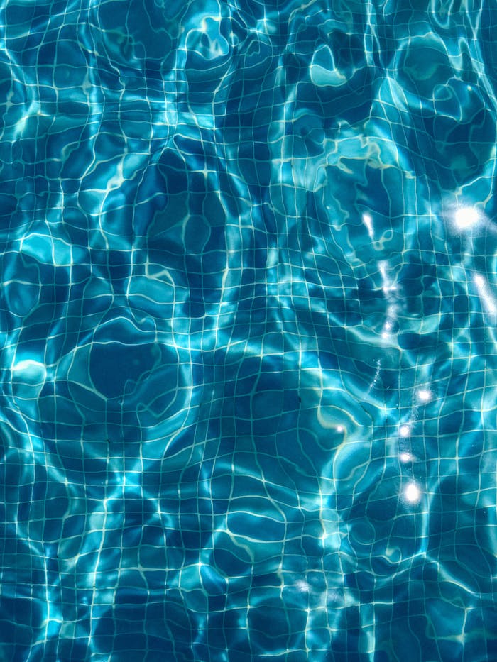 Abstract view of sunlit ripples in a clear blue swimming pool featuring tile patterns.